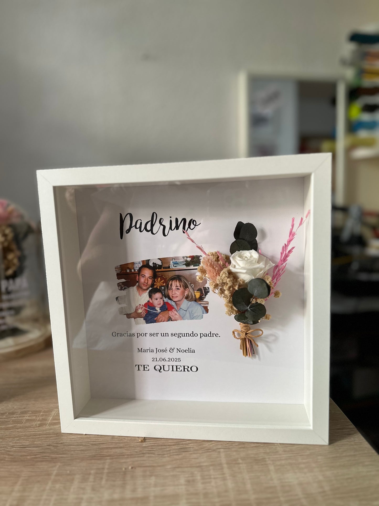 Cuadro con texto, flores preservadas y fotografía.